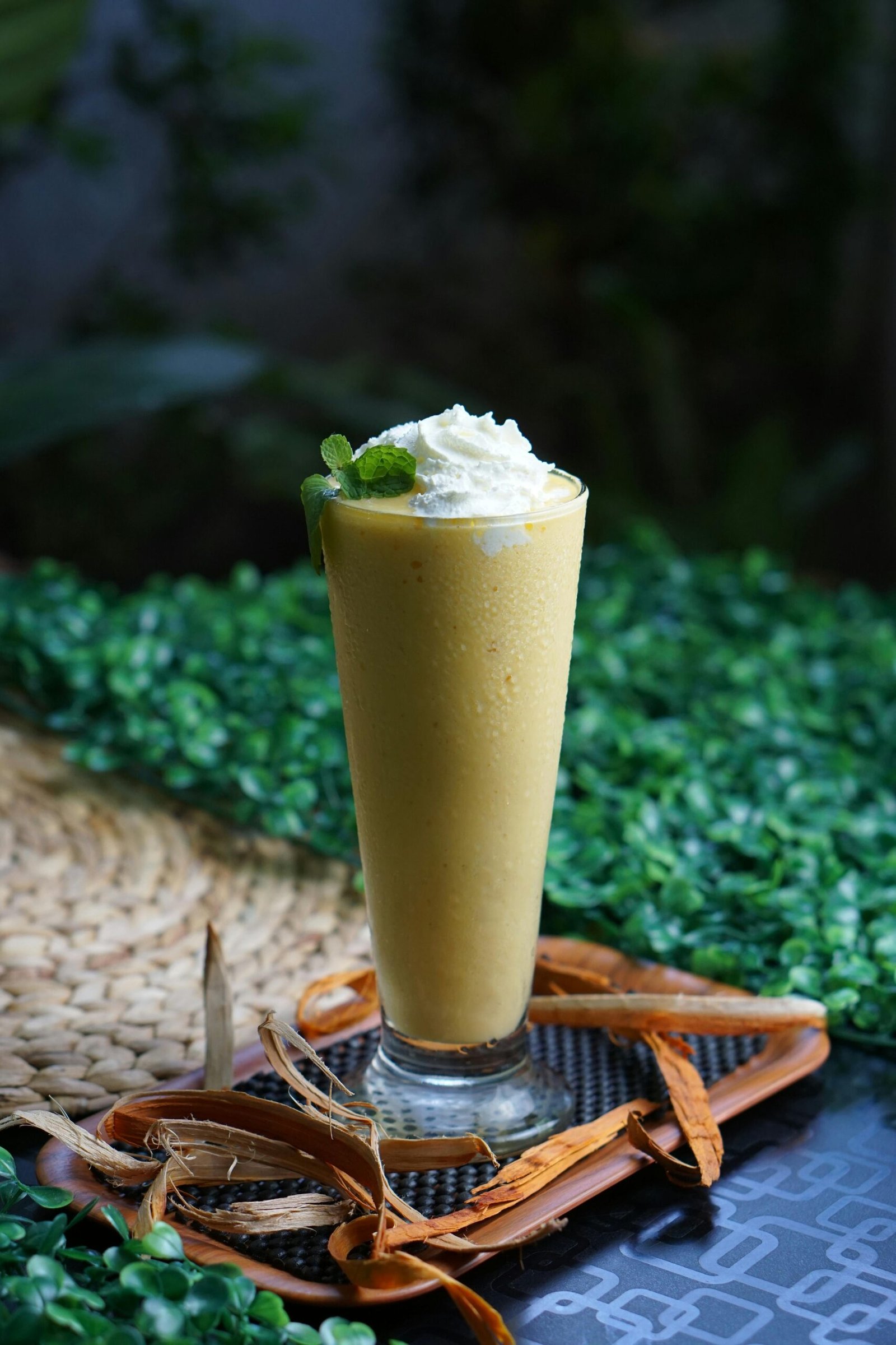 Tall mango smoothie topped with whipped cream on a decorative tray outdoors.