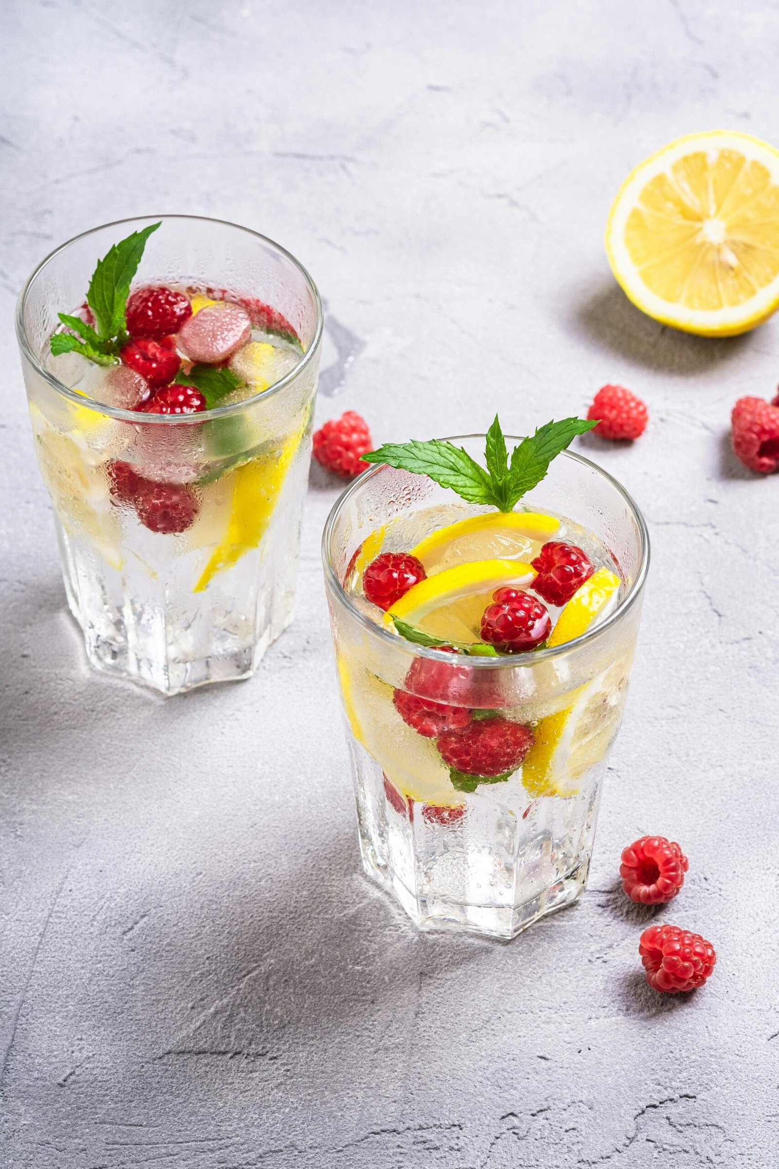 Refreshing summer drink with lemon, raspberries, and mint in glasses.